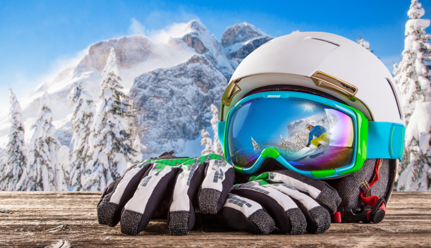 Colorful ski glasses, gloves and helmet on wooden table. Winter ski theme.